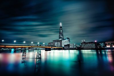 Bridge over thames river with reflection against modern buildings at night