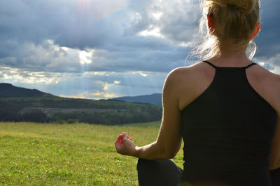 Lady is meditating in a mountain field faced to the sun behind stormy sky on west in the afternoon