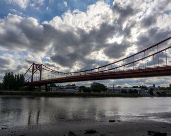 View of suspension bridge over river against cloudy sky