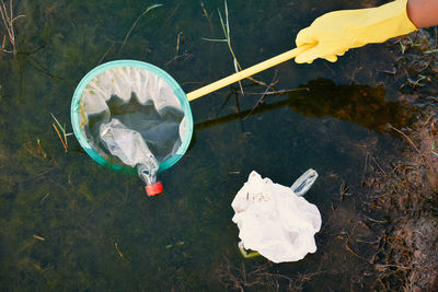Cropped hand removing bottle from net floating in lake