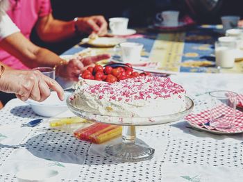 Cropped hand cutting birthday cake on table