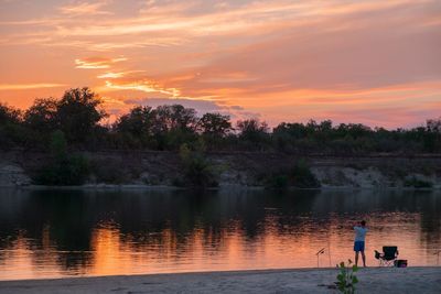 Silhouette people standing by lake against sky during sunset