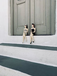 Full length of young woman with arms raised against wall