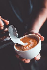 Midsection of barista pouring milk in coffee at cafe