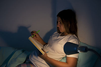 Portrait of young woman using mobile phone while sitting on bed at home