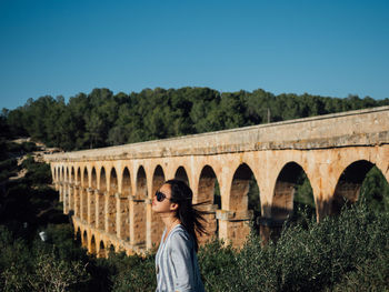 Side view of woman standing against bridge