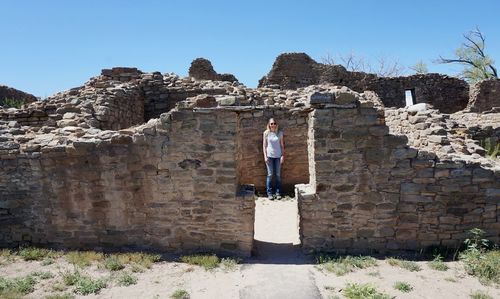 Woman standing by stone wall against clear sky