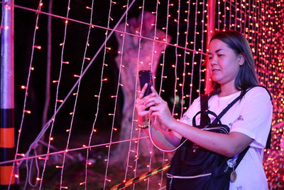 Woman using mobile phone by illuminated lighting equipment at night