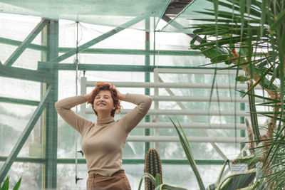 A beautiful plus size girl enjoying standing among the green plants of the greenhouse.