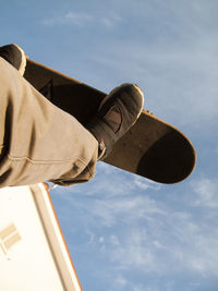 Low section of skateboarder performing stunt against sky