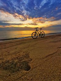 Bicycle on beach against sky during sunset