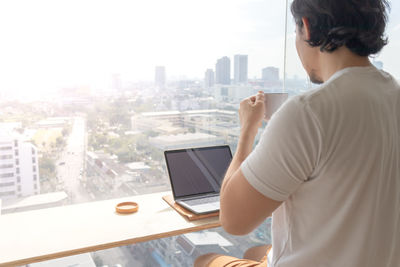 Rear view of man using digital tablet while standing in office