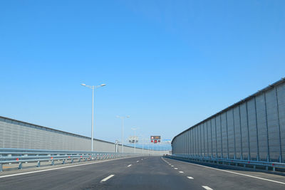 Road by bridge against clear blue sky