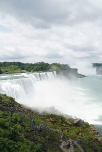 Scenic view of waterfall against cloudy sky