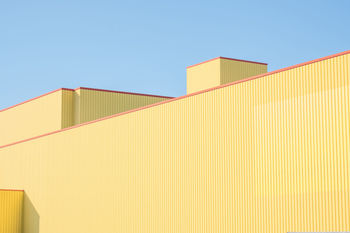 Low angle view of yellow factory building against clear blue sky