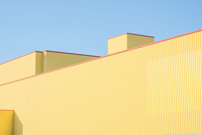 Low angle view of yellow factory building against clear blue sky
