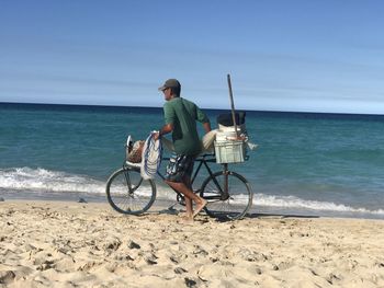 Side view of man carrying bicycle at beach