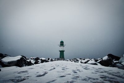 Lighthouse by frozen lake against clear sky