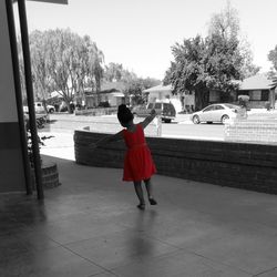 Rear view full length of girl in red dress with arms outstretched outside building