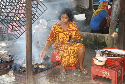 Portrait of young woman sitting on barbecue grill