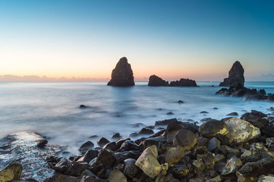 Rocks on beach against sky during sunset