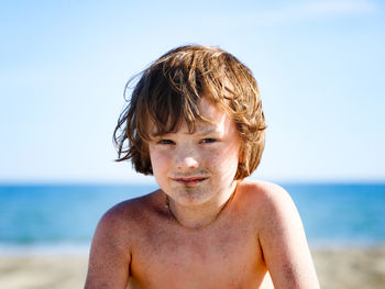 Portrait of shirtless boy at beach against sky
