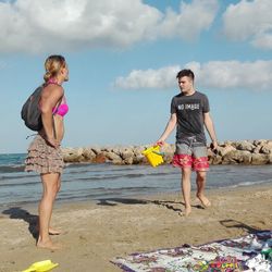 Friends talking while standing at beach against sky