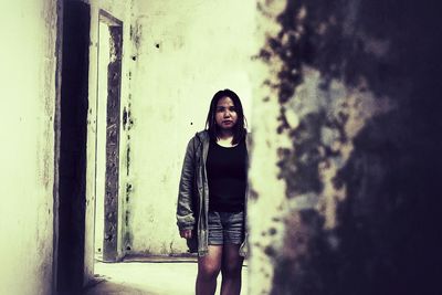 Portrait of young woman standing against wall