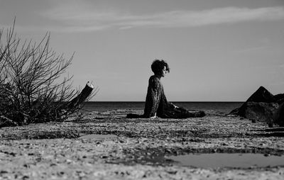 Side view of woman sitting on beach against sky