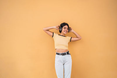 Smiling young woman standing by wall while listening music