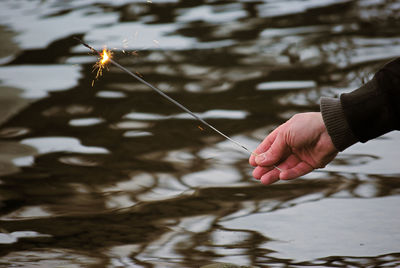 Cropped hand holding sparkler over lake