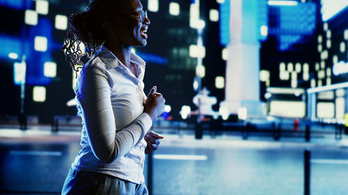 Side view of young woman standing in city at night