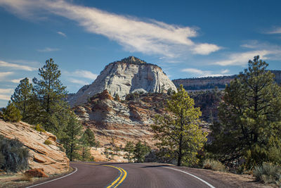 Road amidst trees and mountains against sky