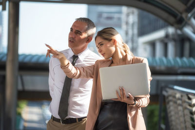 Businesswoman pointing away while standing with businessman on footbridge