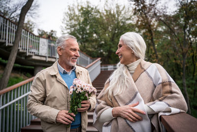 Smiling man holding bouquet standing with woman against trees