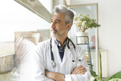 Thoughtful doctor with arms crossed looking out through window