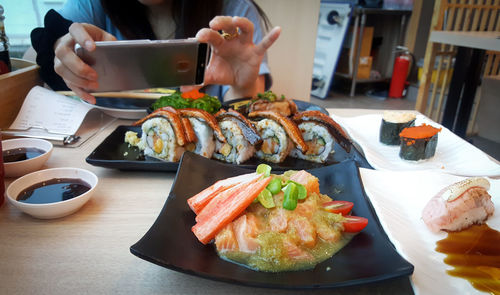 Midsection of woman photographing food with mobile phone served on table in restaurant