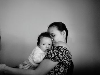 Portrait mother carrying daughter against wall