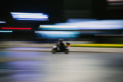 Blurred motion of man riding motorcycle on road at night