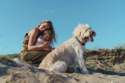 Woman with child and a dog sitting on land against sky