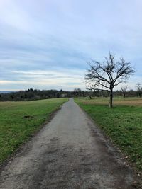 Empty road amidst field against sky