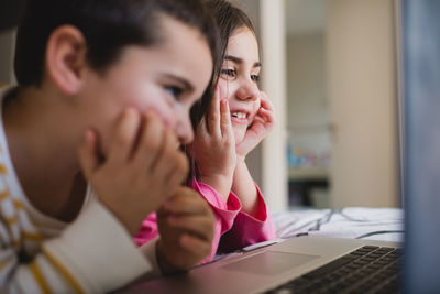 Happy little sister and brother having fun and playing game on laptop together while spending free time in bedroom at home