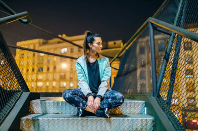 Happy young woman athlete wearing casual sportswear sitting on a metallic stairs at night