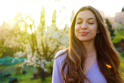 Beautiful young woman with eyes closed against trees