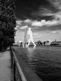 Statue by river in city against sky