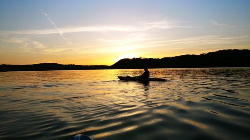 Silhouette man on boat in sea against sky during sunset