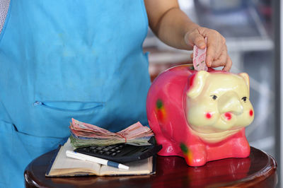 Midsection of person inserting paper currency in piggy bank