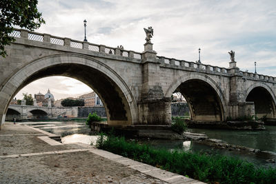 Arch bridge over river against cloudy sky