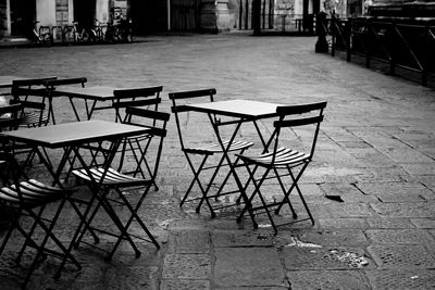 Empty chairs and tables at sidewalk cafe against building