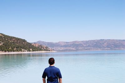 Rear view of man looking at lake against clear sky